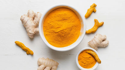 Turmeric powder in a white bowl with fresh turmeric roots on a light background